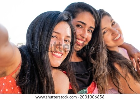 Three latin friends taking a picture of themselves outdoors in a sunny day. Happy hispanic girl friends smiling at camera taking a photo for her social media. Women in summer fashionably dressed.