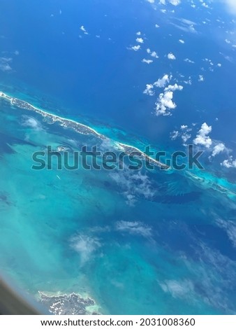 Picture of small island in the middle of ocean, surrounded by small clouds.