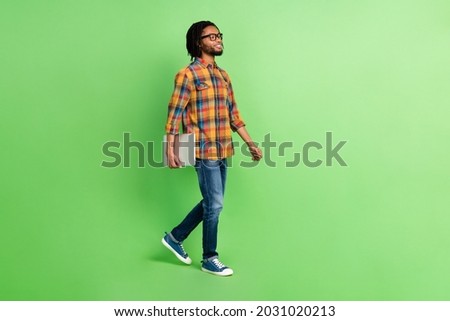 Photo of sweet confident dark skin guy dressed shirt glasses walking holding modern device empty space isolated green color background