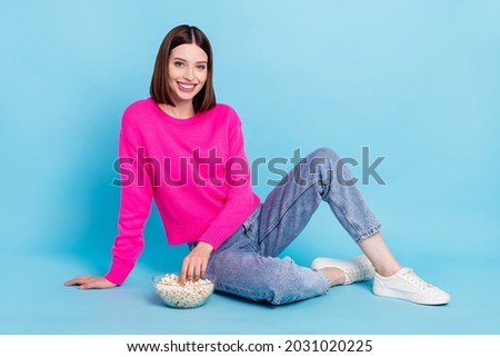 Photo of adorable sweet young lady wear pink pullover sitting floor eating pop corn isolated blue color background