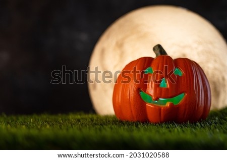Halloween background. Smiling orange pumpkin on a green meadow, illuminated from the inside with green light. Night black sky and large white moon. Minimalism.Empty space to insert.