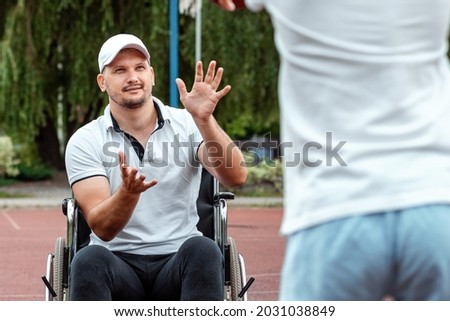 A man in a wheelchair plays basketball with his son on the sports ground. Disabled parent, happy childhood, disabled person concept
