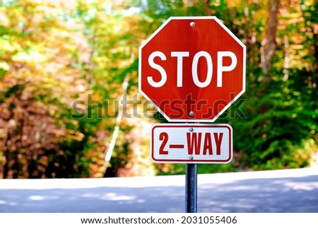 Red 2 way stop sign against road traffic and autumn nature trees. Public transport and traffic control, stop sign background.