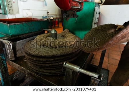 Operator stacking fiber disks in machine applying crushed olive paste for pressing on artisanal olive oil factory