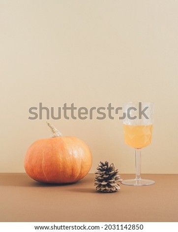 Retro style aesthetic concept with a pumpkin, pine and drinking glass on pastel brown background. Creative 2021 Halloween and autumn idea, minimalistic vertical arrangement.