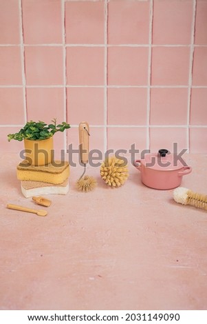 Natural eco friendly bamboo cleaning brushes, sponges, kitchen utensils, casserole dish and a green plant in a yellow pot on a pink tile background. Royalty-Free Stock Photo #2031149090