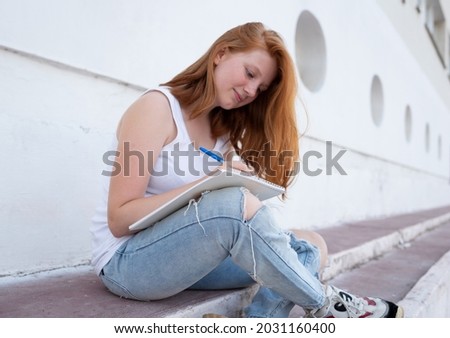 teenage girl draws in the sketchbook while sitting on the steps.