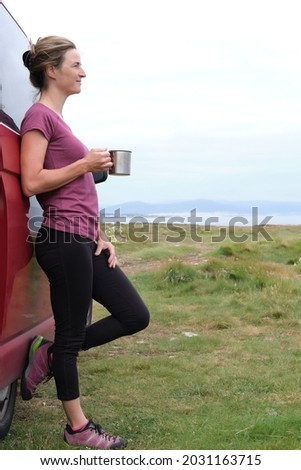 Woman holding a cup in her hand next to her campervan on her summer holiday.