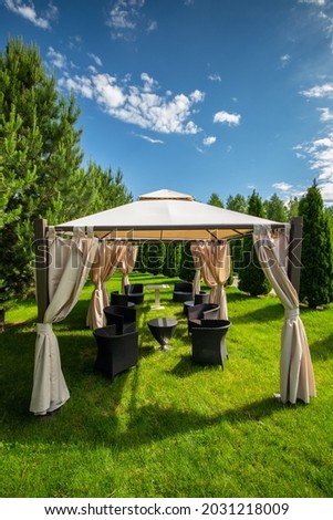 White canvas gazebo with plastic garden furniture in a summer green lawn. Vertical, copy space. Royalty-Free Stock Photo #2031218009