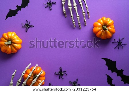 Halloween decorations, pumpkins, spiders, bats on violet background. Flat lay, top view, copy space. Halloween greeting card mockup.