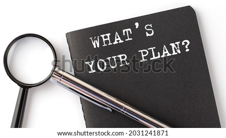 WHAT'S YOUR PLAN - business concept, magnifier with white text message on the black notebook
