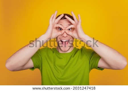 Close up photo of young man show finger okey symbol near eye binoculars childish isolated yellow bright background