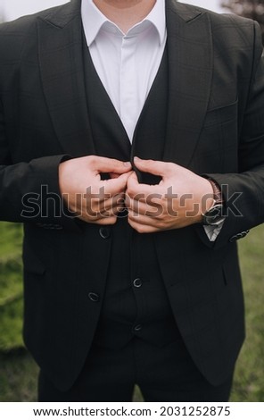 Stylish man, businessman buttons buttons on a black suit with his hands. Business photography.