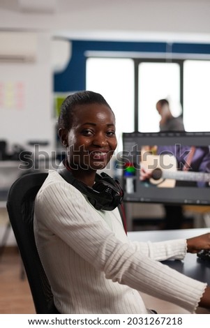 African american video editor artist looking at camera smiling editing creative video project in post production software working in startup studio office. Videographer editing audio film montage