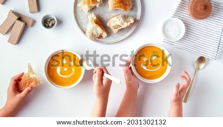 Children eat pumpkin cream soup with cartoon smiles from cream, no face Royalty-Free Stock Photo #2031302132