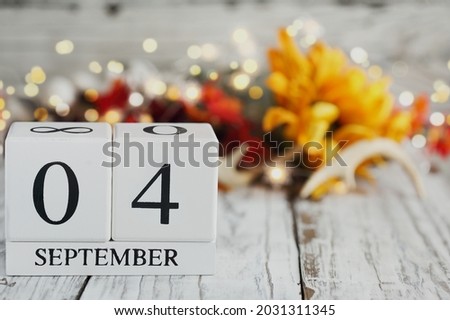 White wood calendar blocks with the date September 4th and autumn decorations over a wooden table. Selective focus with blurred background. 
