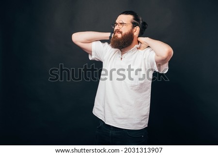Frustrated man is touching his neck and shoulders because they hurt. Photo made in a black backgrounded studio.