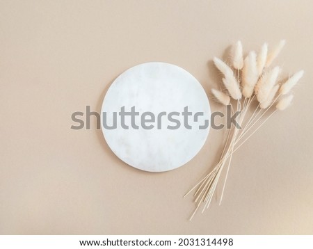 Marble white round podium and bouquet of dry Lagurus on beige background. Place, background for cosmetics. Top view. Copy space
