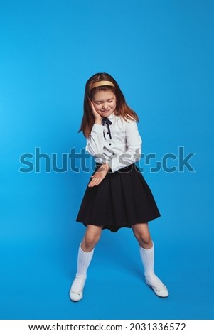 Back to school and happy time. Funny schoolgirl playing and act like dj over blue paper wall background. Kid in school uniform have fun in studio