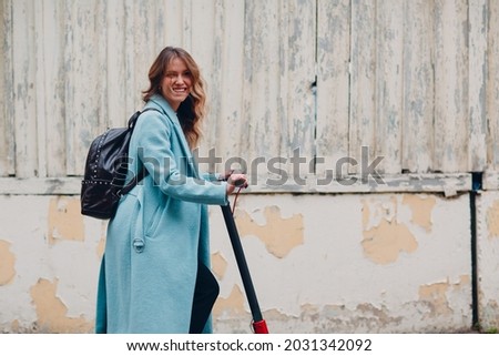 Young woman with electric scooter in blue coat outdoor city