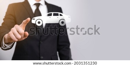 Male hand holding car auto icon on grey background. Wide banner composition.Car automobile insurance and collision damage waiver concepts.