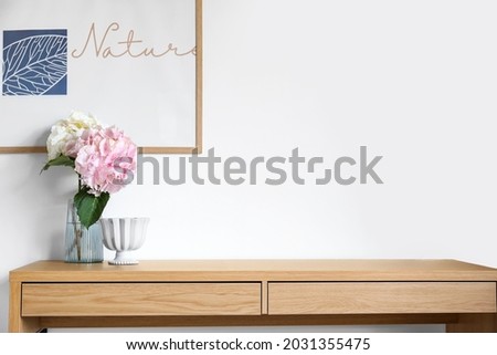 Vase with beautiful hydrangea flowers and decor on table near light wall