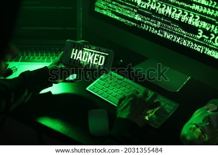 Hacker with mobile phone using computer in dark room