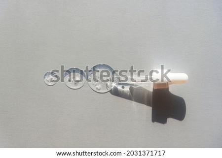 Three drops of hyaluronic acid and pipette on light gray background in sunlight. Top view, flat lay.