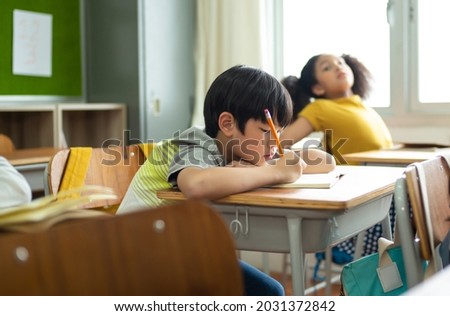 Unhappy Schoolboy studying in classroom at school during lesson, bored and discouraged student. School children education habit concept.
