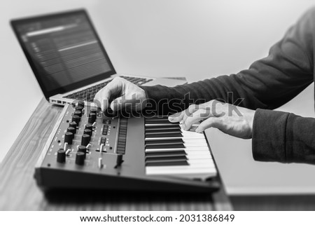 male music producer, composer hands playing synthesizer keyboard for recording midi and audio tracks on laptop computer in home studio