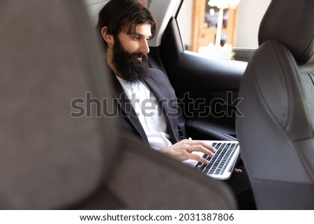 Businessman working in the drivers seat in his car. Young man using devices and gadgets. Making reports, analitycs, routine processing tasks. Concept of business, finance, professional occupation.
