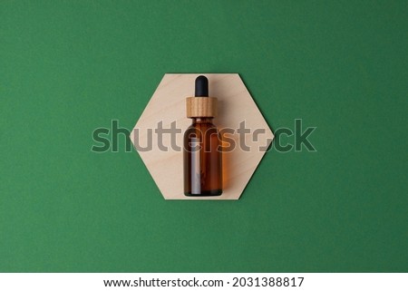 Cosmetic bottle with a wooden hexagon on green background. Flat lay, copy space