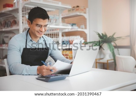 Entrepreneur male business owner in eyeglasses using computer laptop working in grocery shop store Royalty-Free Stock Photo #2031390467