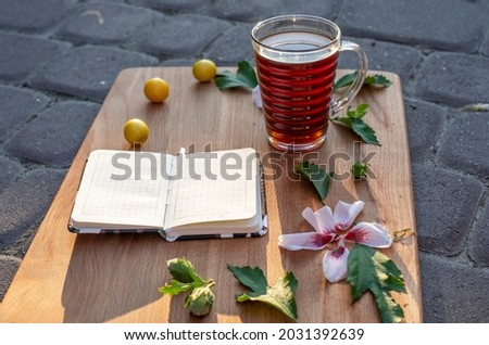 good morning, hot drink with cherry plum, with crumbs, pink hibiscus petals and a notebook on a blackboard on a stone surface, horizontal