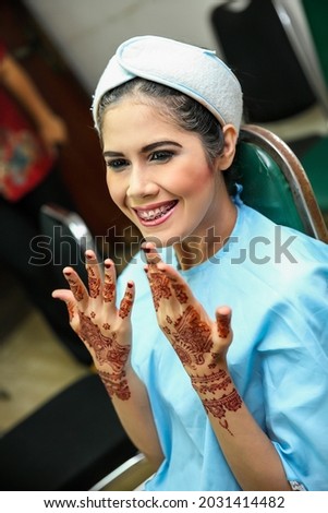 Portrait of beautiful young Asian female model smiling and showing hands with henna tattoo after make up by professional artist. For fashion and wedding background. Cheerful and happy expression. 