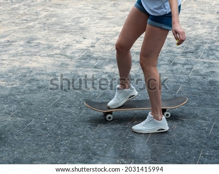 Close up photo of cool young girl with beautiful legs in white sneakers riding skateboard in shiny summer day . Outdoor activities. Street culture.