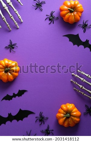Halloween poster with festive decorations, pumpkins, spiders, skeletons hands, bats on purple background. Flat lay, top view, overhead.