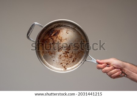 Dirty oily burnt metal frying pan held in hand by male hand. . Royalty-Free Stock Photo #2031441215
