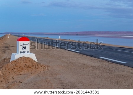 Milestone post on the Tozeur highway written in French and Arabic. Road passes through salt lake of Chott el Djerid, Tunisia. Royalty-Free Stock Photo #2031443381