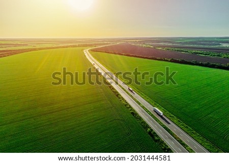 two white trucks driving on asphalt road along the green fields at sunset. seen from the air. Aerial view landscape. drone photography. cargo delivery
