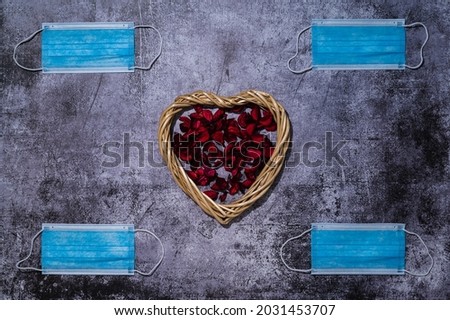 A heart-shaped straw frame with dry red petals inside is depicted on a marble background, four medical masks are symmetrically arranged in the corners
