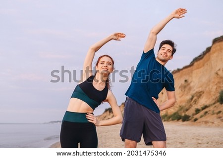 Couple young two friend strong sporty sportswoman sportsman woman man in sport clothes warm up tilt hand body to sides stretch exercise on sand sea ocean beach outdoor seaside in summer day morning Royalty-Free Stock Photo #2031475346