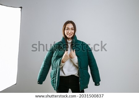 girl in a green jacket posing in a photo studio on a gray background