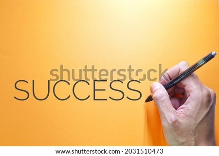 Success text words typography, Business Concept, Motivational concept. Marketing and Communications Concept. A man's hand writes Success, High angle view. Top view. Flat lay. Orange Background