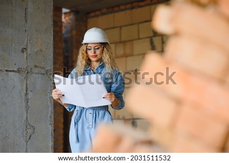 Construction concept. Pretty female builder in overalls and helmet working on construction site.