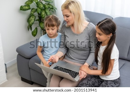 Homeschool young two little daughters learning internet online do homework by using computer with mother help, teach and encourage. Girl and baby sister happy to study education at home together