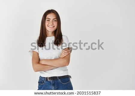 Confident young female student standing with crossed arms and smiling at camera, posing over white background