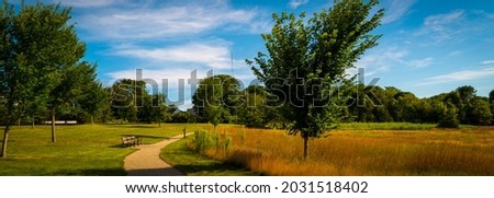 Nature park with curved footpath and benches. Bright autumn day with white clouds over the brown grasses in the meadow.