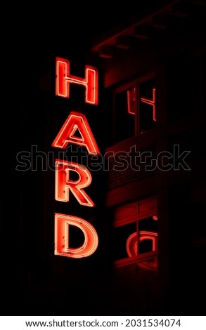 Neon sign "hard" illuminated with a reflection in the window behind it