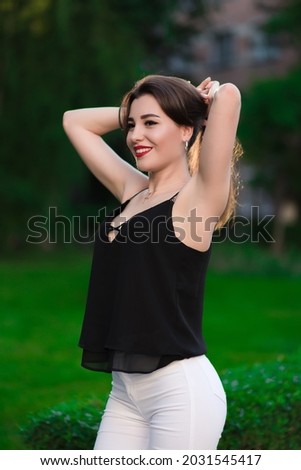 A beautiful girl in white pants and a black sweater posing against a background of flowers. Fashion concept. Lifestyle